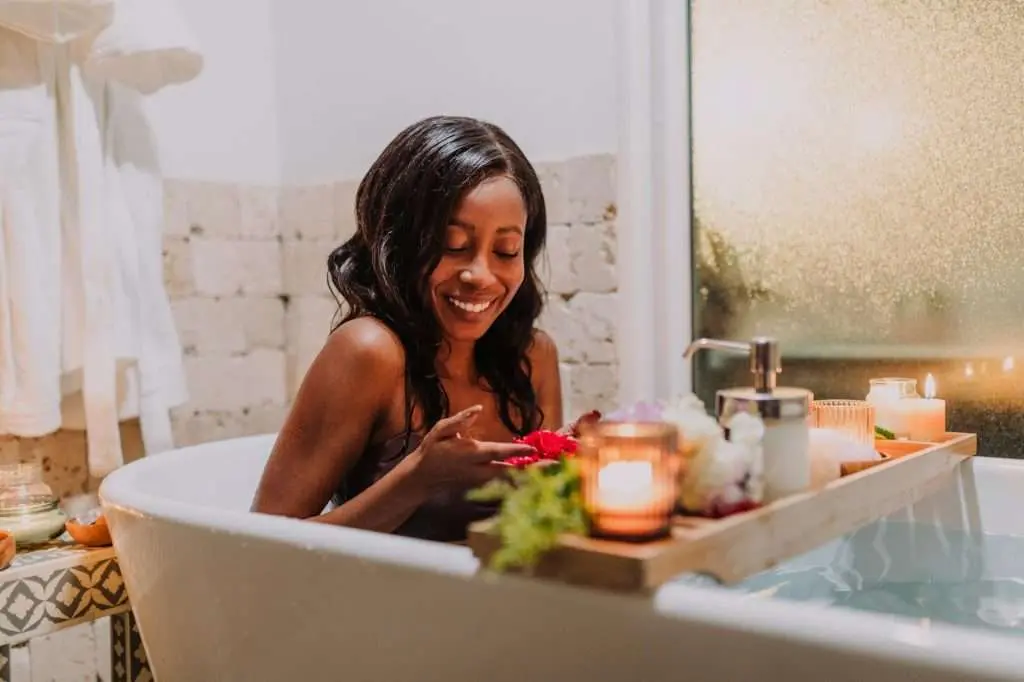 a woman sitting in a bathtub with a wooden tray with candlelights